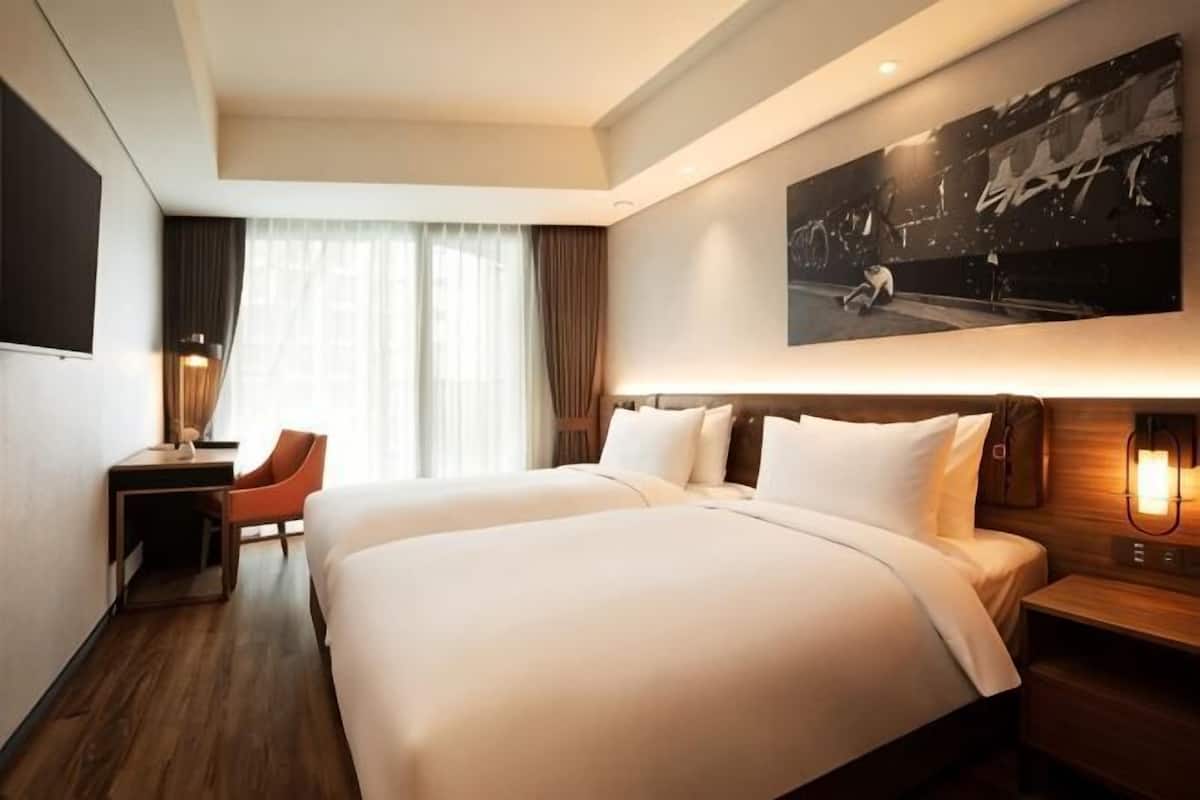 Habitación de hotel con dos camas, un escritorio, una silla y un cuadro grande en la pared.