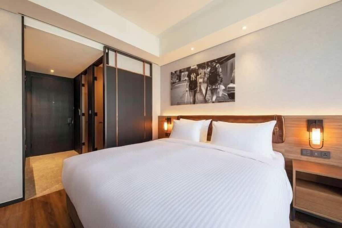 Una habitación de hotel con una cama grande, un armario, una mesita de noche y una lámpara fijada en la pared.