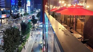 A modern urban hotel with a balcony overlooking a busy street at night.