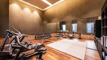 Academia com equipamentos de ginástica, um espelho grande e piso de madeira.