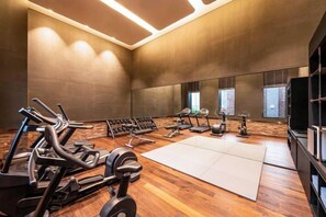 Ein Fitnessraum mit Trainingsgeräten, einem großen Spiegel und Holzboden.