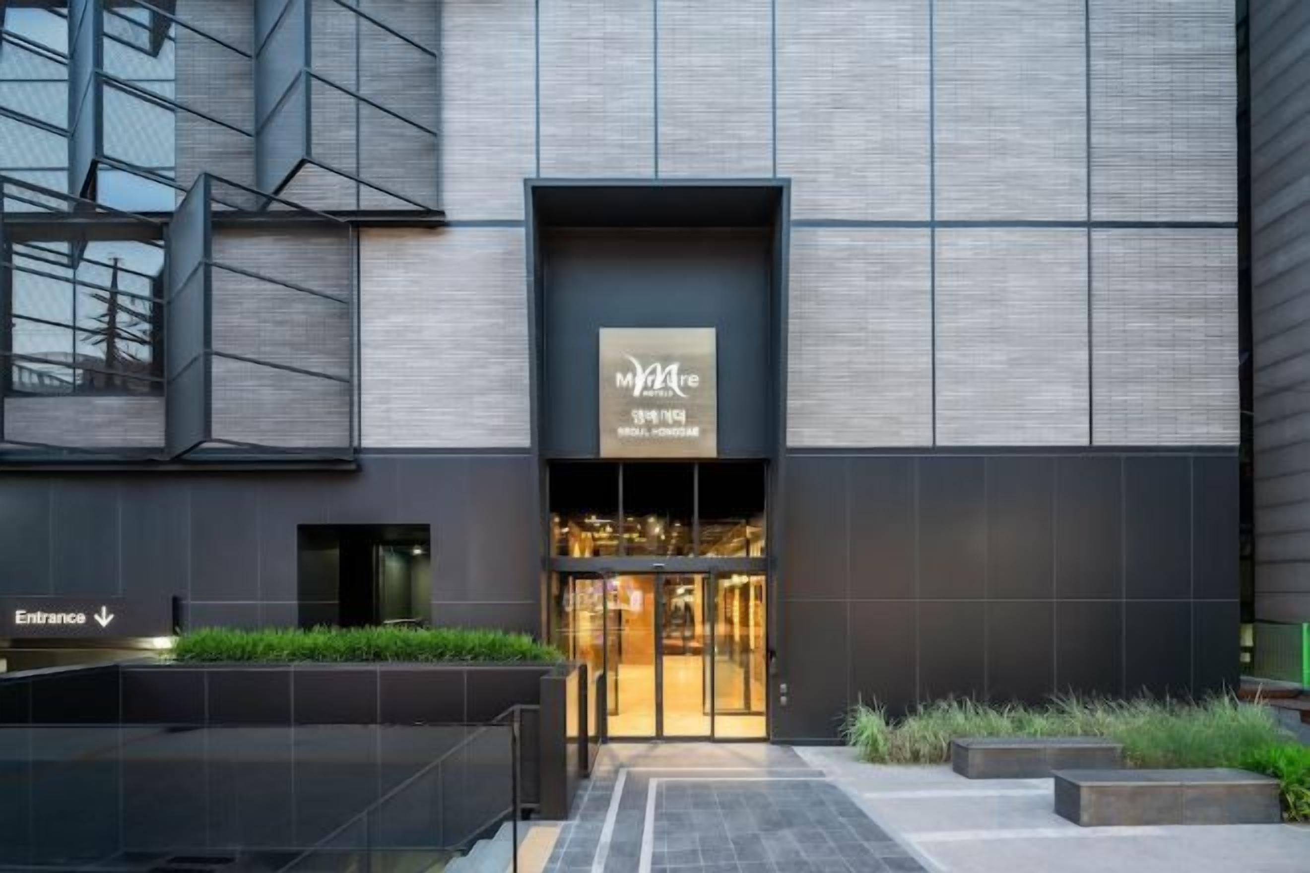 Un edificio moderno con una entrada destacada, un cartel sobre la puerta y un camino que conduce a la entrada.