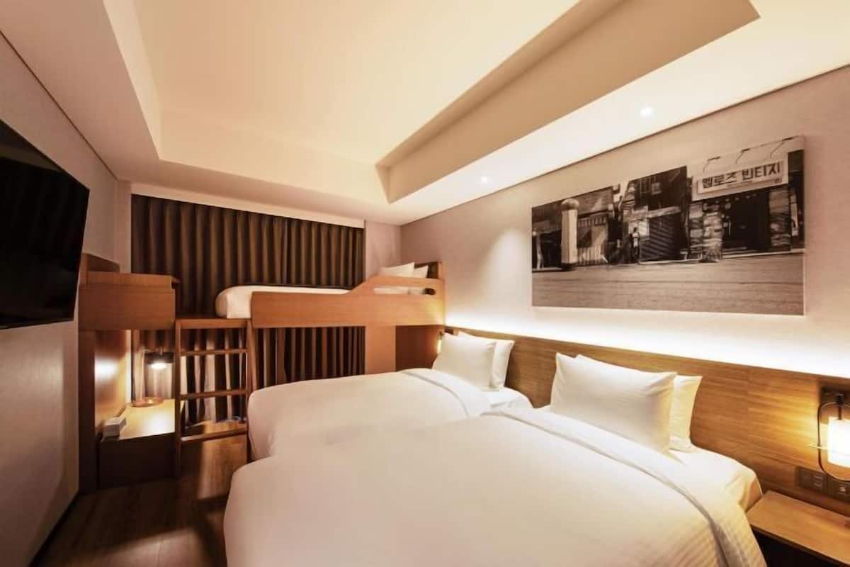 Una habitación de hotel moderna con una cama litera, una cama grande, un televisor montado en la pared y un cuadro enmarcado sobre la cama.