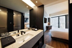 A modern hotel bathroom with a large sink, a mirror, and a bed with a view of the city. - Mercure Ambassador Seoul Hongdae (Seoul)