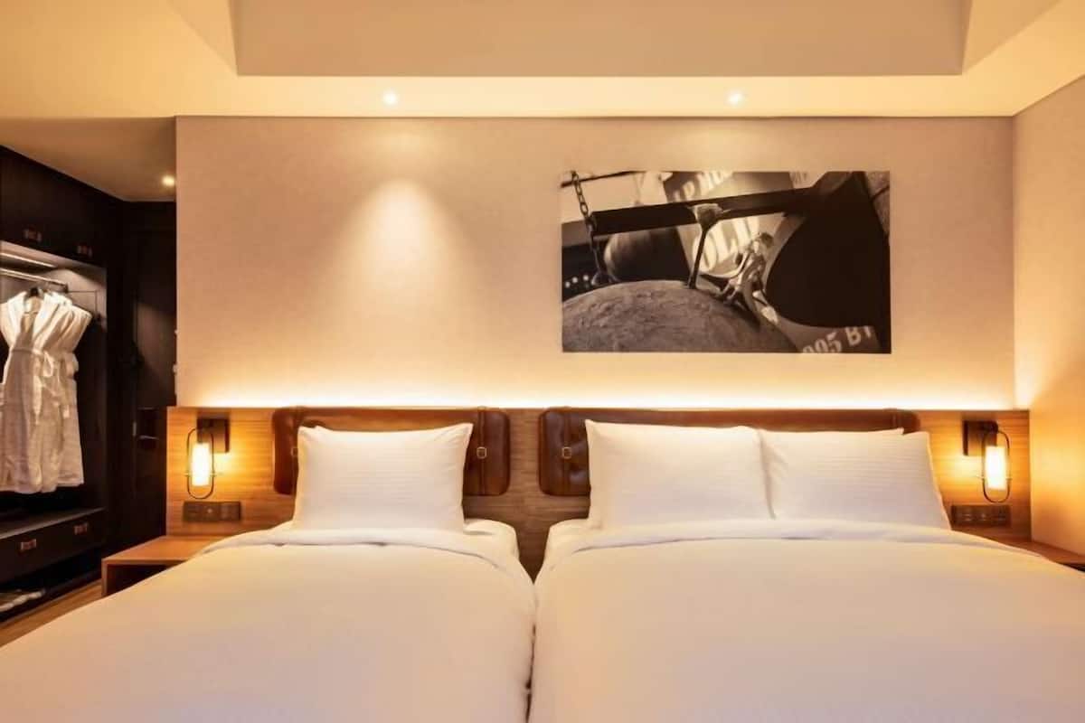 Habitación de hotel con dos camas, un cuadro grande en la pared y un armario.