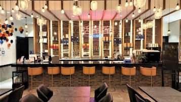 Uma área de bar com balcão, banquetas e luminárias pendentes.