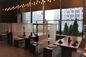 A modern interior with tables and chairs, large windows, and a view of buildings.