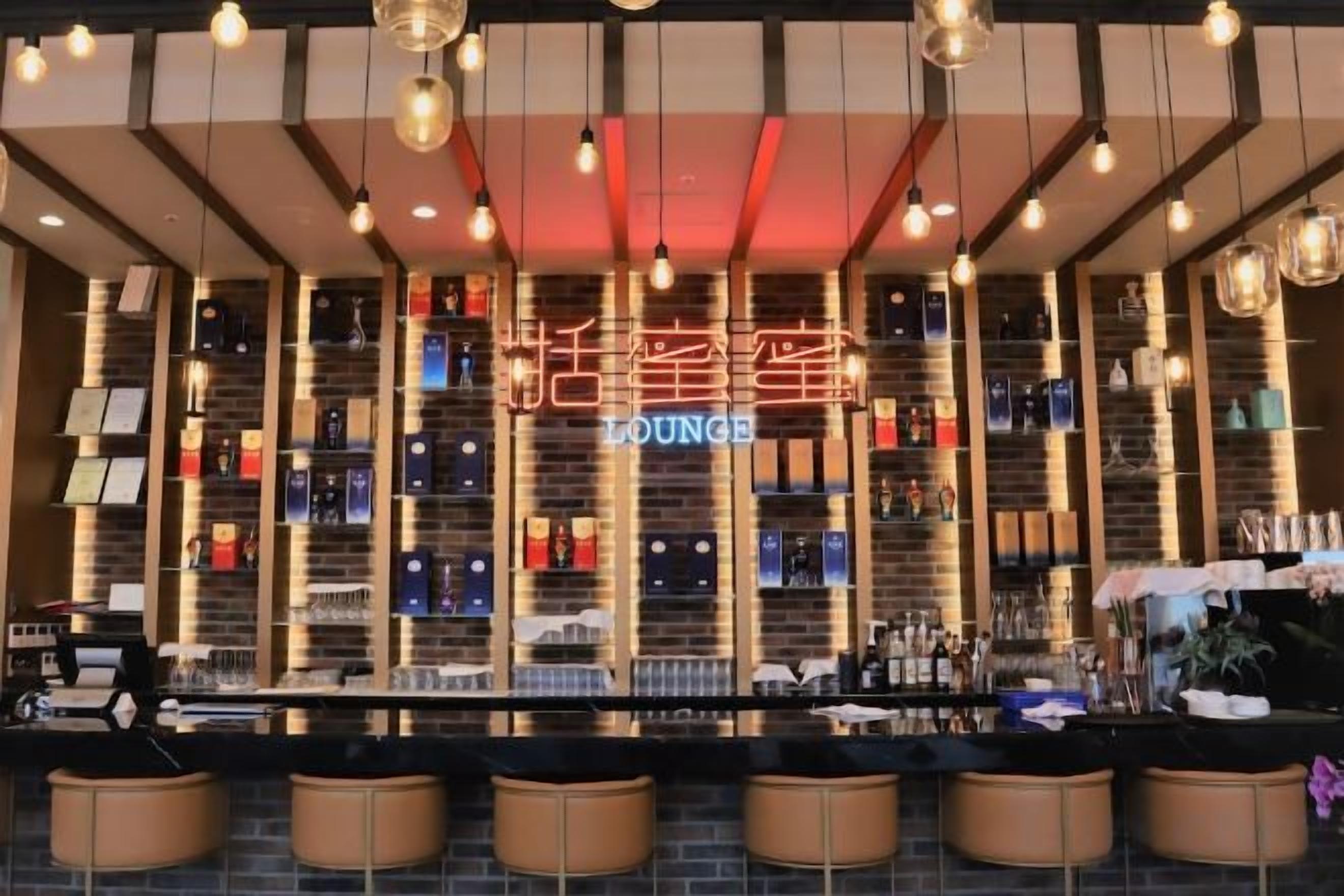 Un espace bar agrémenté d’un panneau indiquant « Lounge », d’étagères remplies de bouteilles et d’un comptoir avec des tabourets de bar.