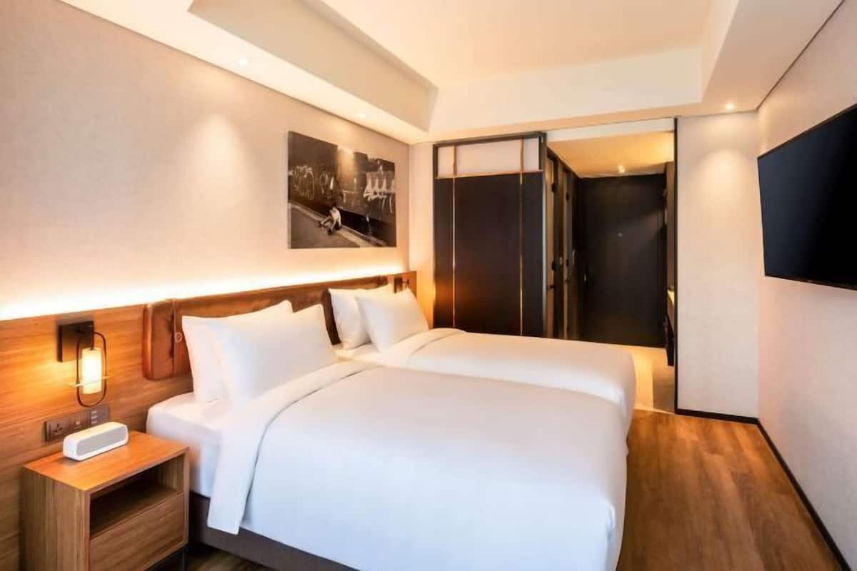 Una habitación de hotel moderna con una cama grande, mesita de noche y un televisor montado en la pared.