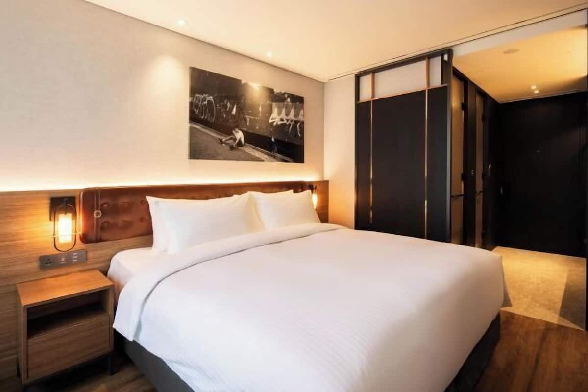 Una habitación de hotel moderna con una cama grande, una mesita de noche, una lámpara de pared y un armario con puerta corredera.