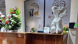 A hotel reception desk with a wooden counter, a floral arrangement, a welcome sign, and a statue of an elephant.