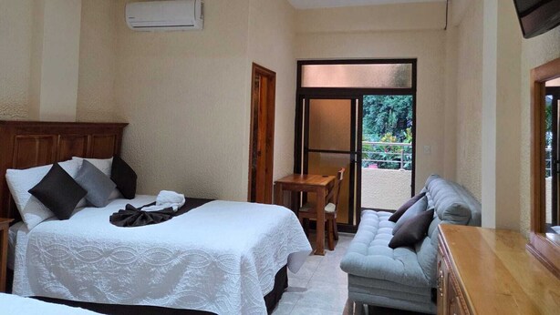 A hotel room with a bed, a sofa, a small table, and a TV.
