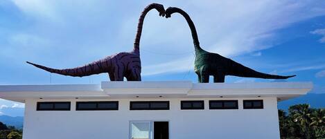Two dinosaur sculptures on a white building with a clear sky.