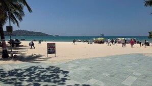 Una spiaggia con una passeggiata lastricata, palme e un cartello segnaletico.