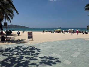 A beach with a paved walkway, palm trees, and a signboard. - ZEN Hotel Patong Beach (Patong)