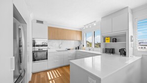 Une cuisine moderne avec des meubles blancs, un grand îlot central et une vue sur l’extérieur.