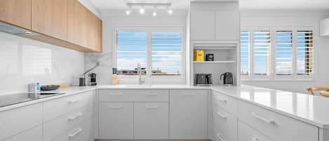 Cocina moderna con muebles blancos, encimera de madera y vistas al mar a través de amplias ventanas.