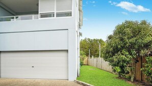 Un bâtiment moderne à deux étages, doté d’un garage fermé, d’une petite cour gazonnée et d’une clôture en bois.