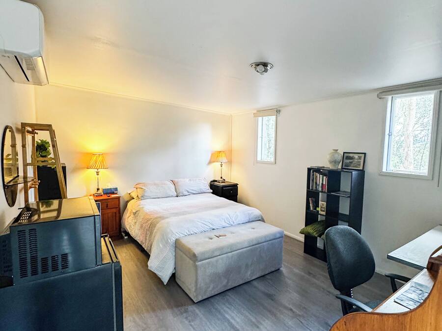 A bedroom with a bed, bedside lamps, a desk, a chair, a bookshelf, and a window.