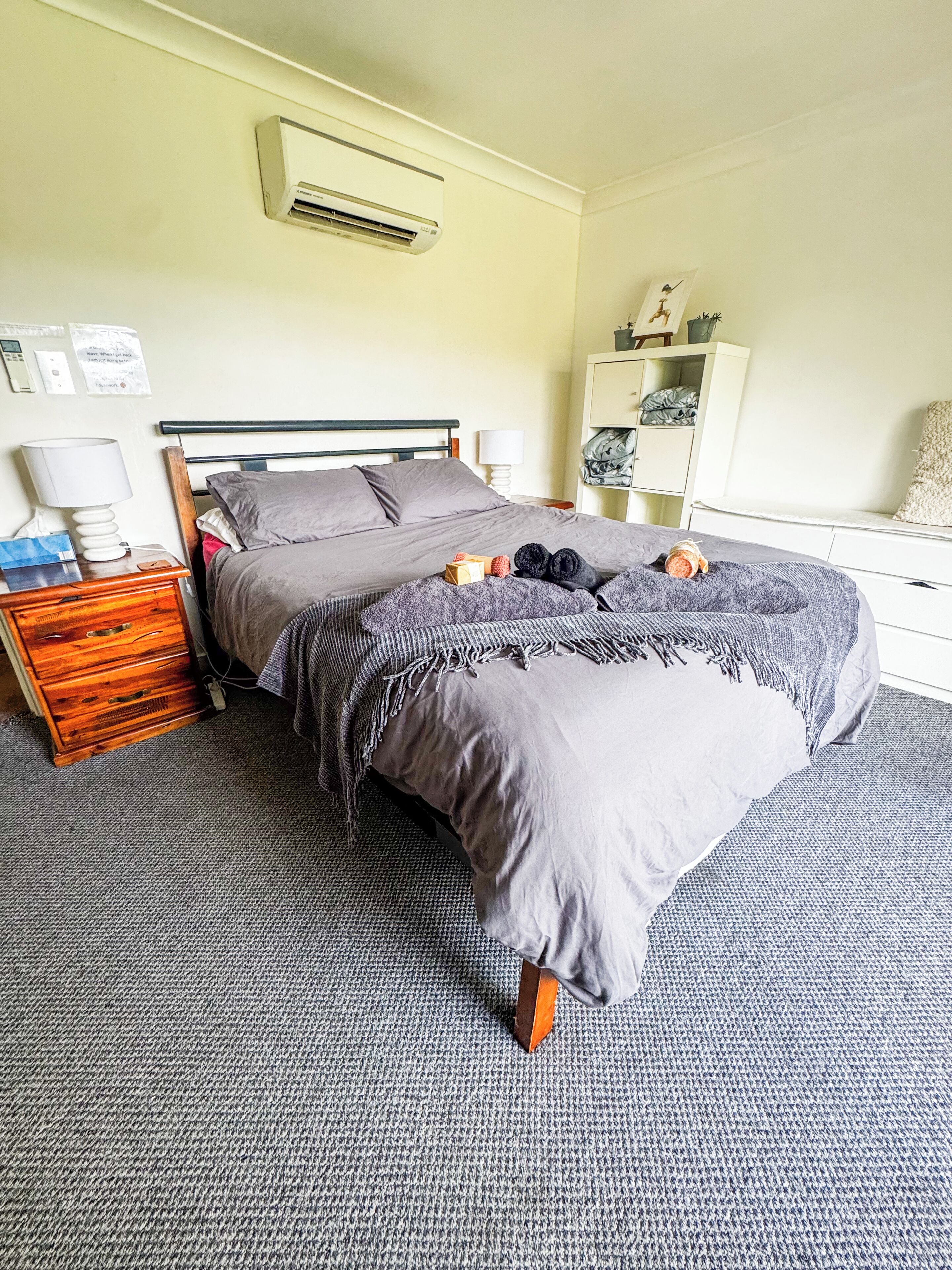 A bedroom with a bed, bedside tables, a wardrobe, and an air conditioning unit.