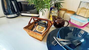 A kitchen counter with a toaster, a coffee maker, a basket of coffee pods, a plant, and various kitchen items.