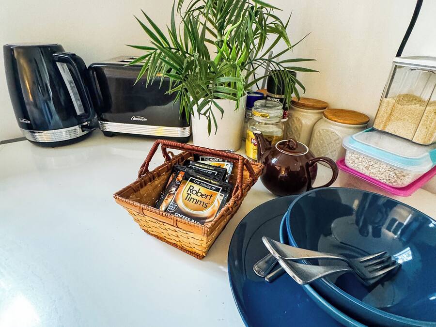 A kitchen counter with a toaster, a coffee maker, a basket of coffee pods, a plant, and various kitchen items.