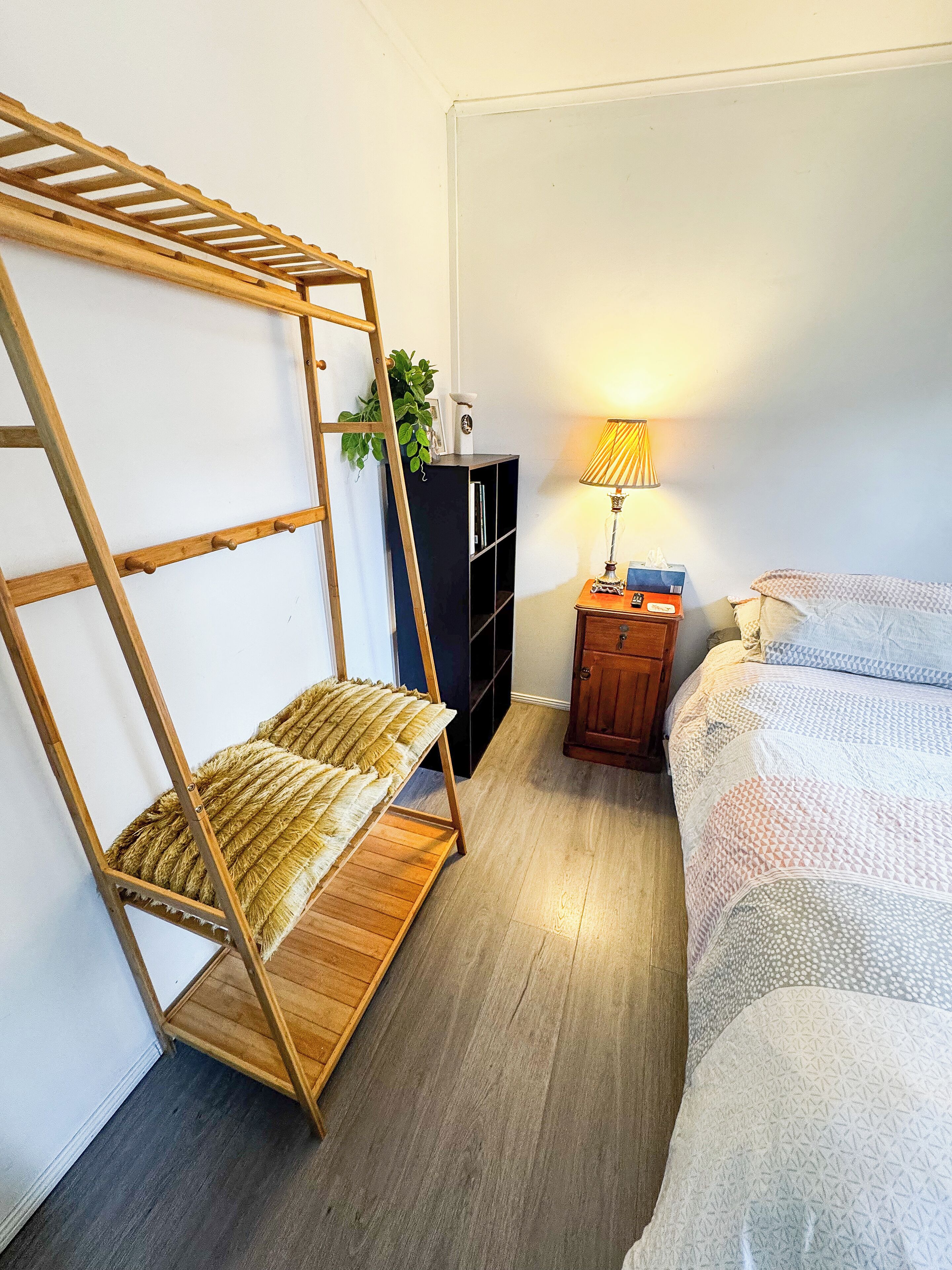 A bedroom with a wooden ladder bed, a small nightstand with a lamp, a black cabinet, and a bed with patterned bedding.