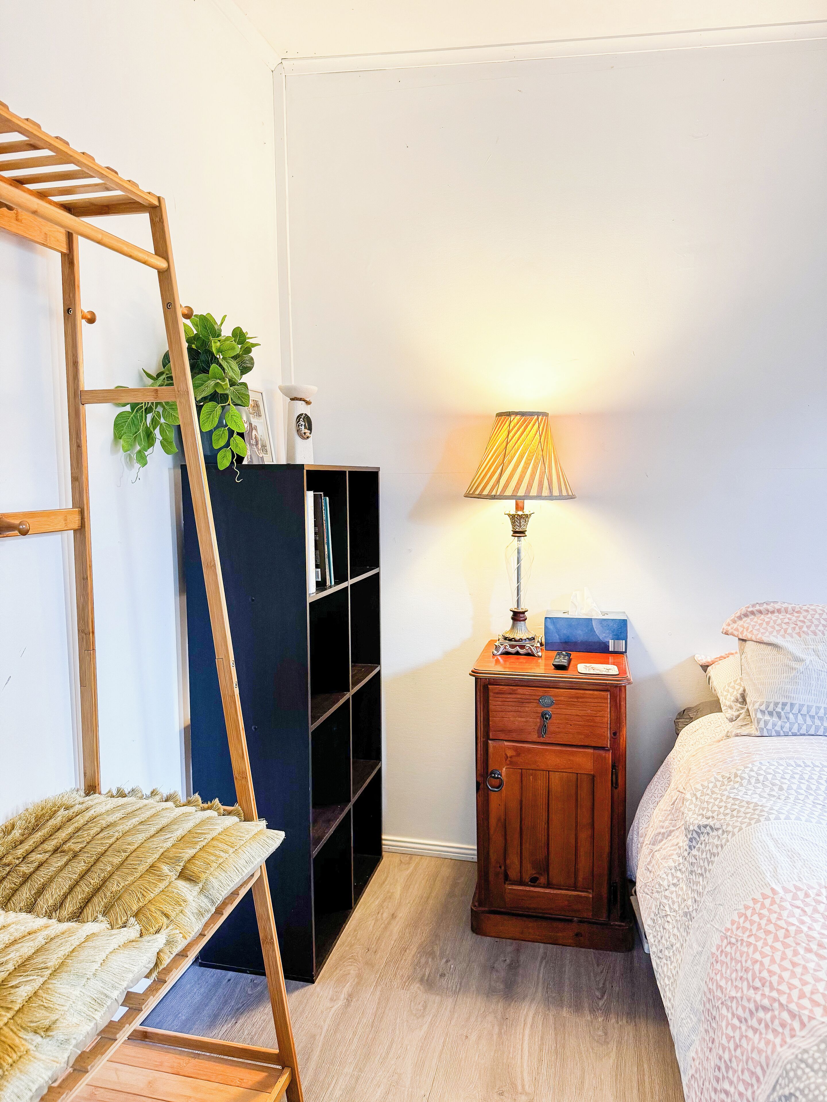 A bedroom with a wooden ladder, a bookshelf, a bedside table with a lamp, and a bed with patterned bedding.