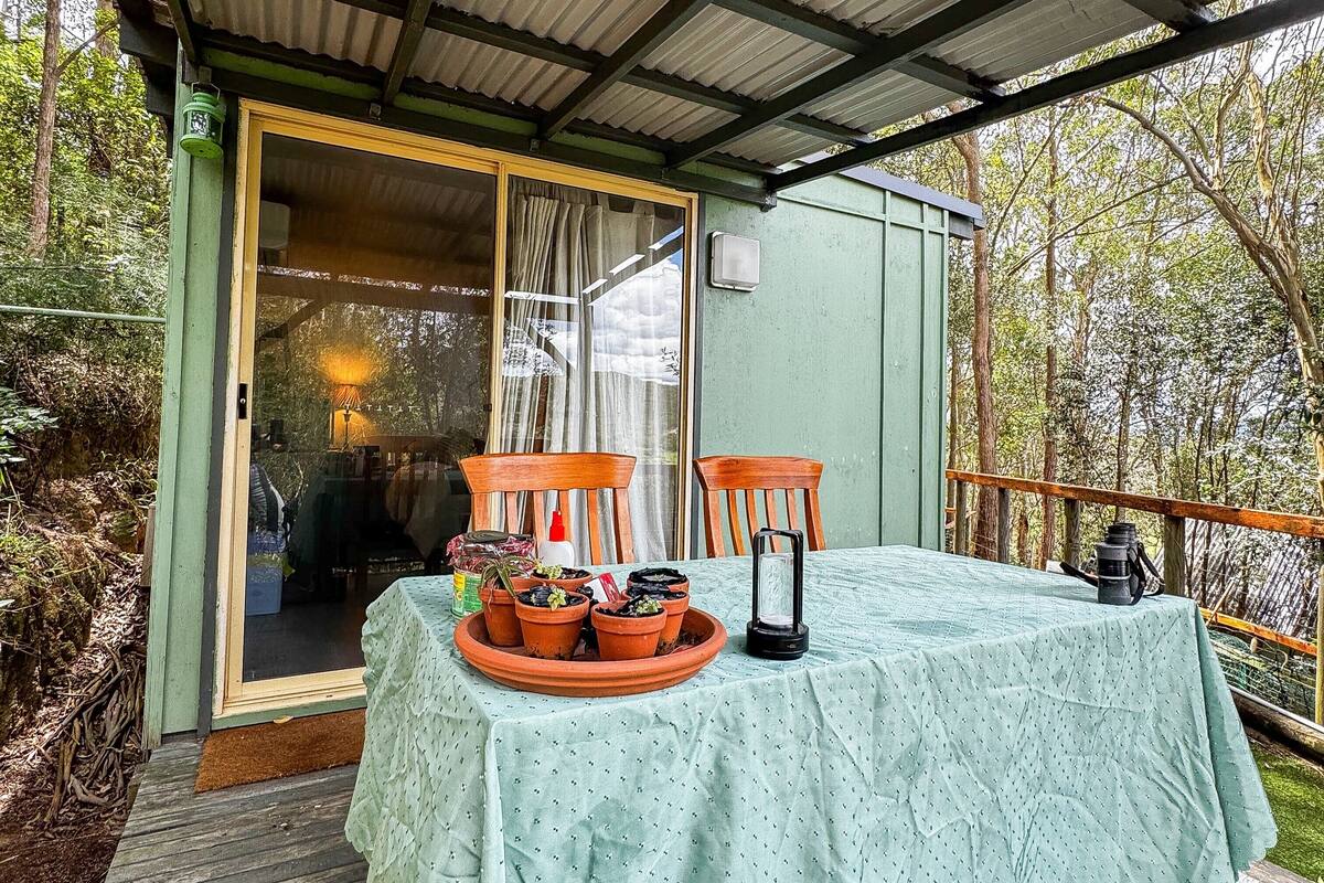 Een klein gebouw met een groen dak, een tafel bedekt met een lichtgroene tafelkleed, omringd door potplanten en een lantaarn.