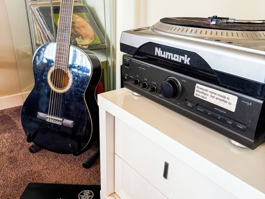 A guitar, a Numark amplifier, and a vinyl record on a white dresser.