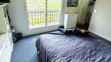 Ein Schlafzimmer mit einem großen Bett, einem Fenster mit Jalousien, einer Deckenleuchte und einem Bild an der Wand.