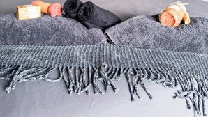 Un lit bien fait, avec une couverture grise et une frange décorative, une petite boîte cadeau et des chaussettes enroulées posées sur le lit.