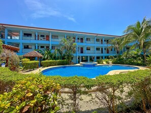 A hotel with a swimming pool, multiple balconies, and lush greenery.