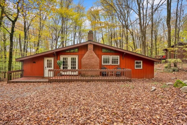 Un chalet rustique avec une cheminée en briques, une terrasse en bois et une forêt en arrière-plan.