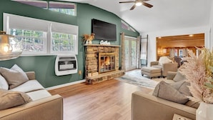 A modern living room with a stone fireplace, a flat-screen TV, and a ceiling fan.