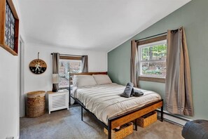 Ein Schlafzimmer mit Bett, Nachttischen, einer Lampe und einem Fenster mit Vorhängen.