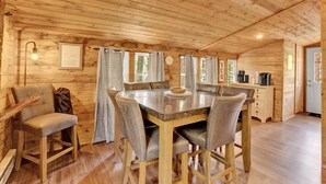 A wooden cabin interior with a dining table, chairs, a sofa, and a coffee station.