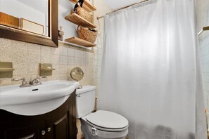 Une salle de bain avec un lavabo blanc, des toilettes, un miroir et des étagères en bois avec des paniers.