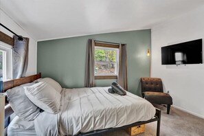 Une chambre à coucher avec un lit, une chaise, un téléviseur fixé au mur et une fenêtre avec des rideaux.