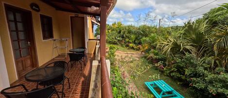 Un porche cubierto con una mesa, sillas, una puerta y vistas a un jardín exuberante con un sendero y bancos.
