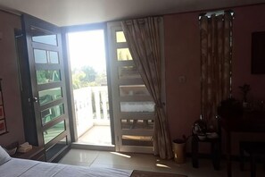A room with a bed, a desk, a chair, a window with curtains, and an open door leading to a balcony. - Hawaii Lounge (Sihanoukville)