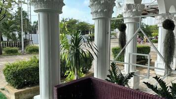 A covered outdoor area with white columns, a wicker bench, and greenery.