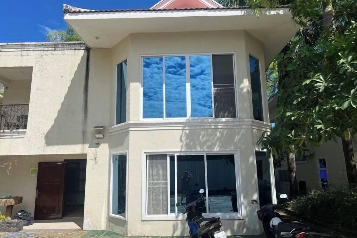 Un immeuble de deux étages doté de grandes fenêtres, d’un balcon et d’un arbre devant.