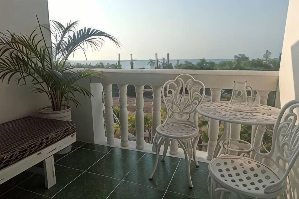 Un balcon doté d’une balustrade blanche, d’un banc en osier et de deux chaises en métal blanc.