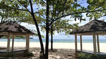 A beach with two gazebos, trees, and a clear view of the ocean.