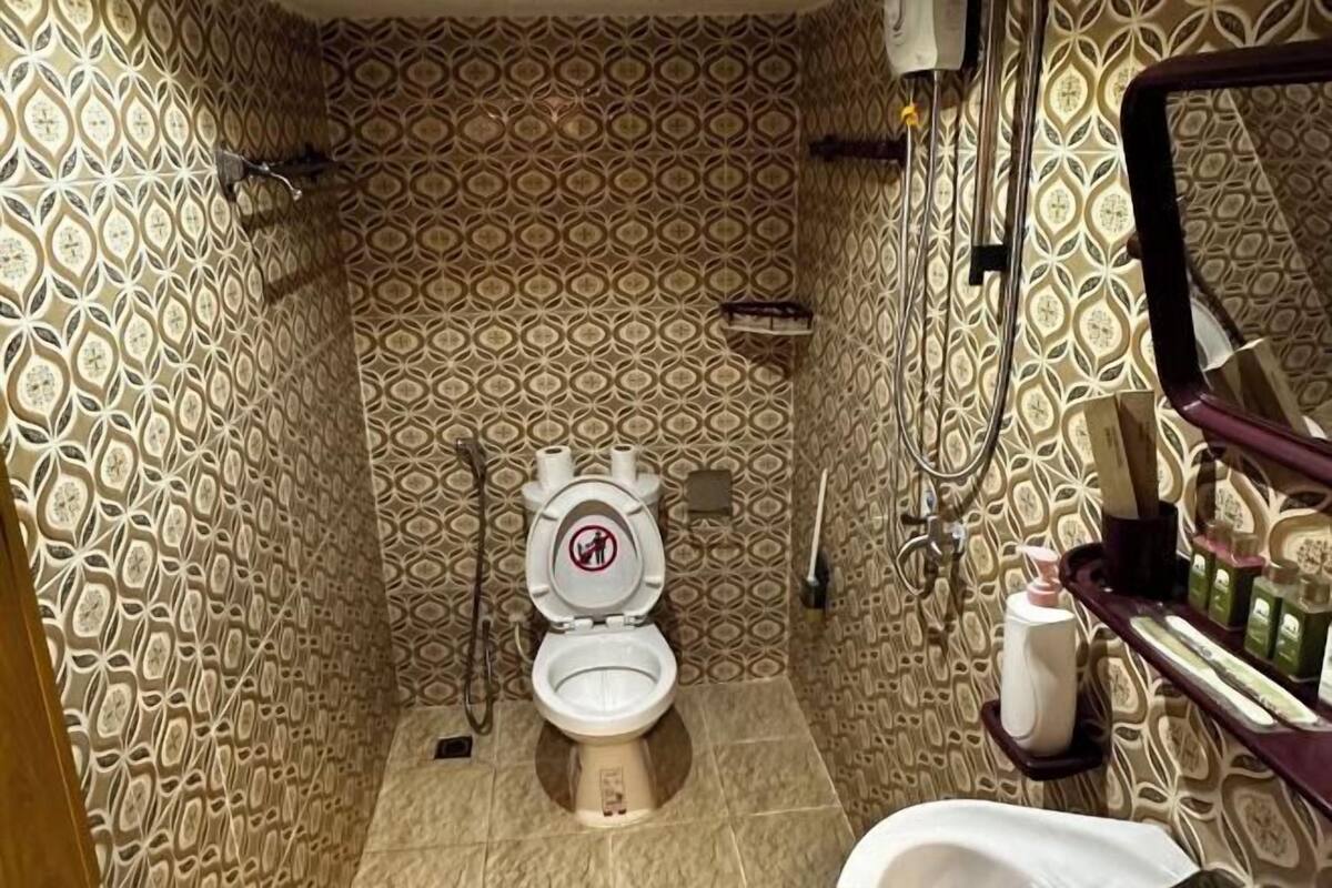 Une salle de bain avec des murs à motifs, des toilettes, un bidet et une étagère contenant des articles de toilette.