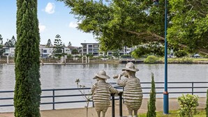 A park with a lake, two stone figures, and a row of buildings in the background. - 2-bed Getaway With Shared Pool & BBQ Access (Brisbane)