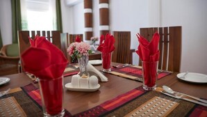 Een eettafel gedekt met rode servetten, een vaas met roze bloemen en een zout- en peperstel.