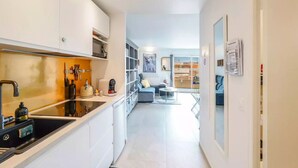 Een moderne keuken met een spoelbak, fornuis en koffiezetapparaat, die uitkomt op een woonruimte met een bank en een eettafel.