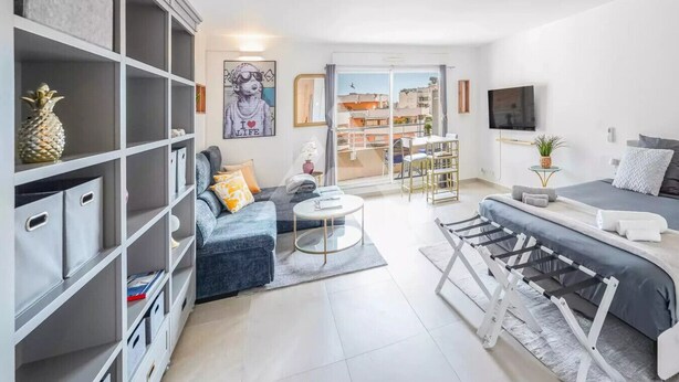 Een moderne woonkamer met een bank, salontafel en televisie. Er is een boekenkast en een eethoek met een tafel en stoelen.
